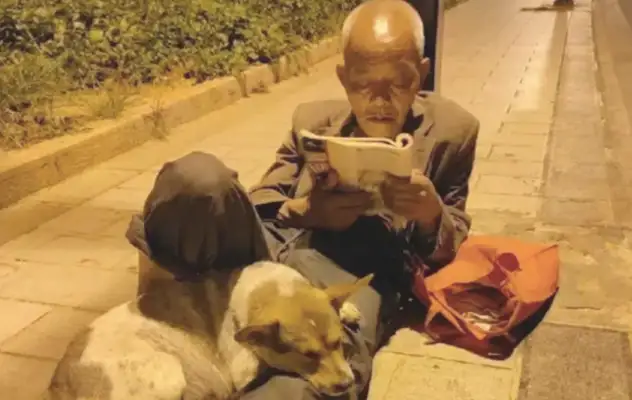 The old man reads under the roadlight, and he's got a puppy on his leg, a dog and a dog. Fan